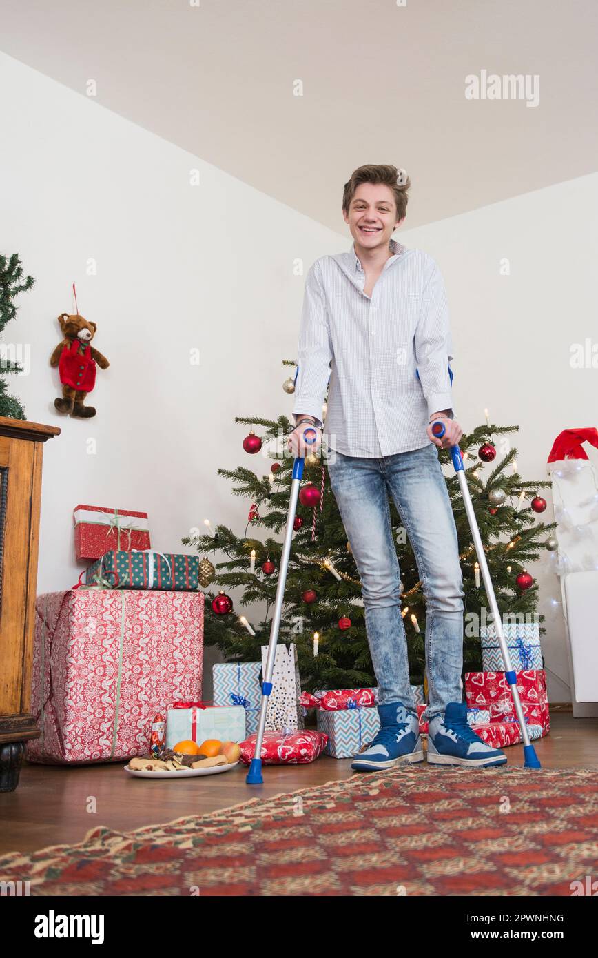 Porträt eines Teenagers, der mit Krücken gegen den Weihnachtsbaum steht Stockfoto