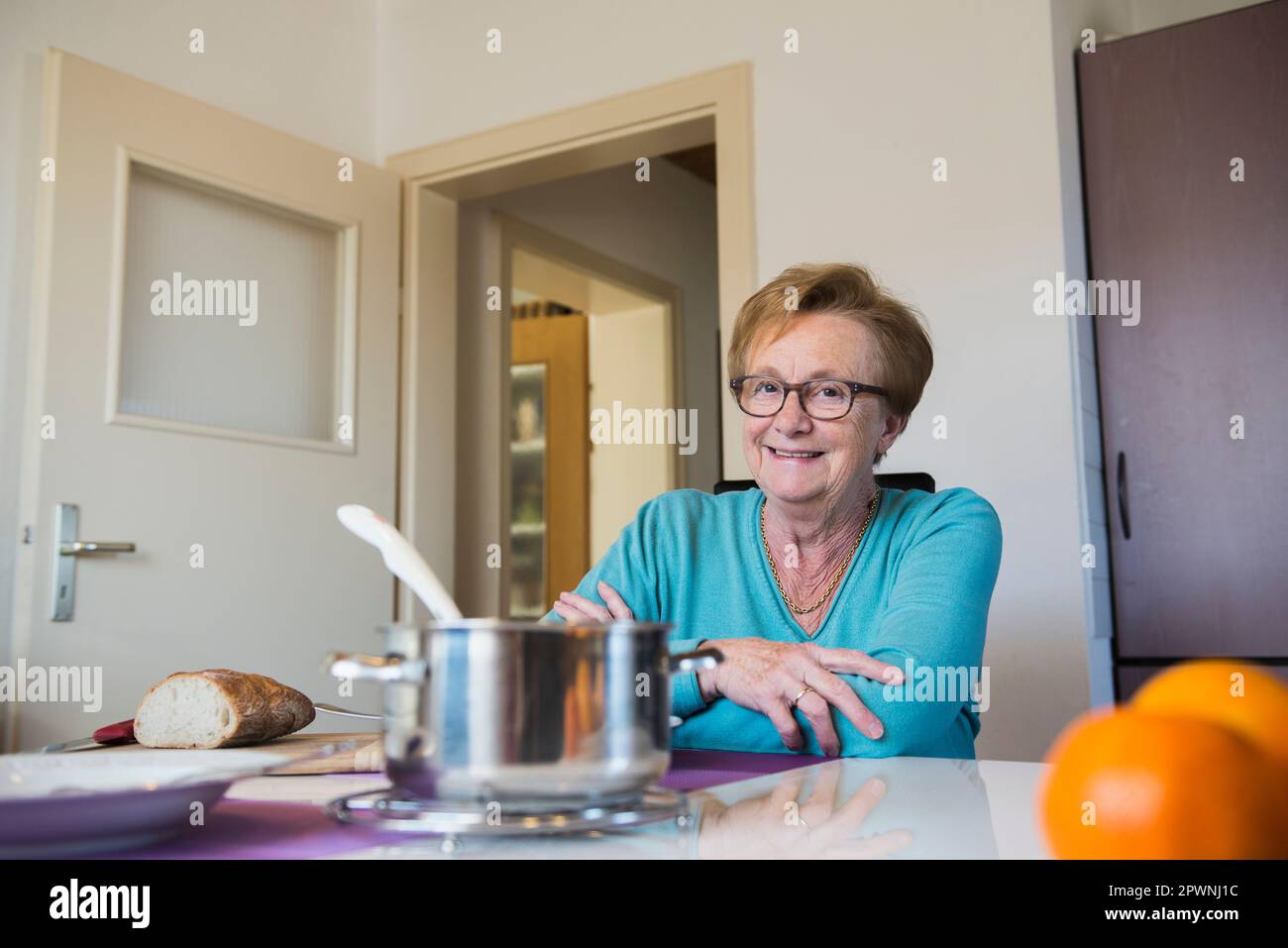 Glückliche alte Frau, die am Esstisch sitzt Stockfoto