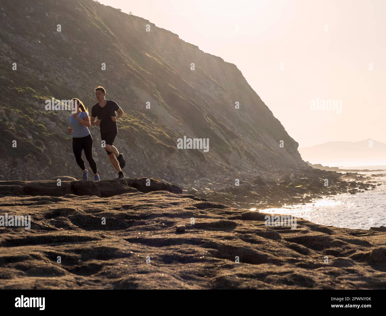 Mann und Frau laufen auf einem einzigen Pfad an der Küste am Strand von Azkorri Stockfoto
