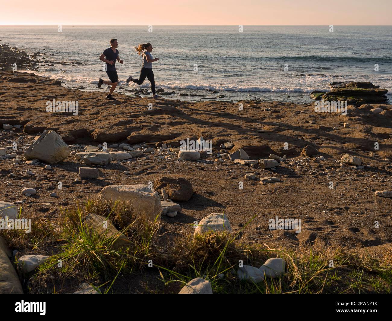 Mann und Frau laufen auf einem einzigen Pfad an der Küste von Azkorri Beach Stockfoto