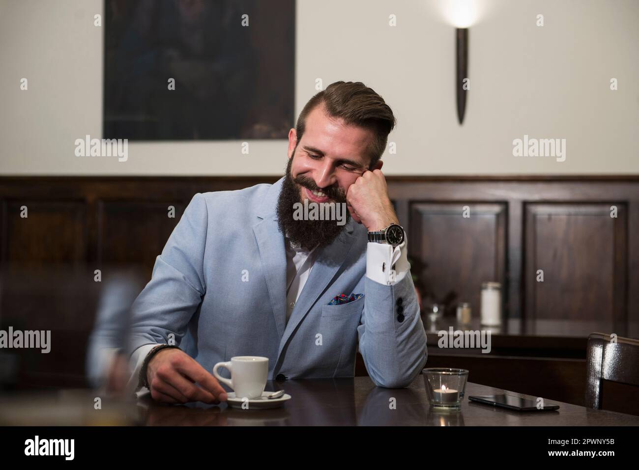 Gut gekleideter Mann, der sich eine Kaffeetasse ansieht und denkt, während er im Restaurant sitzt Stockfoto