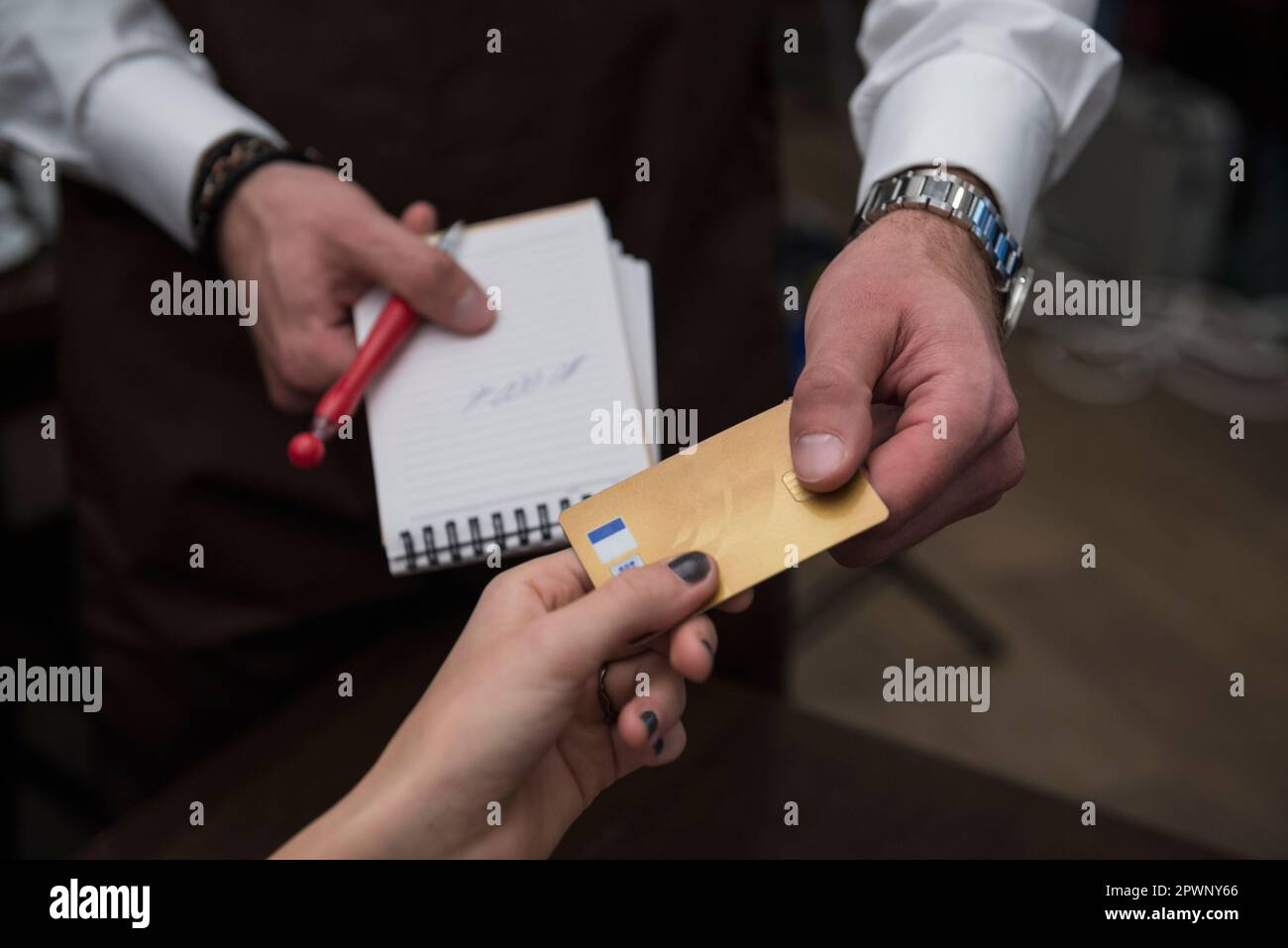 Ein Mann mit Notizblock und Stift, während er Kreditkartenzahlungen von einer Frau annimmt Stockfoto