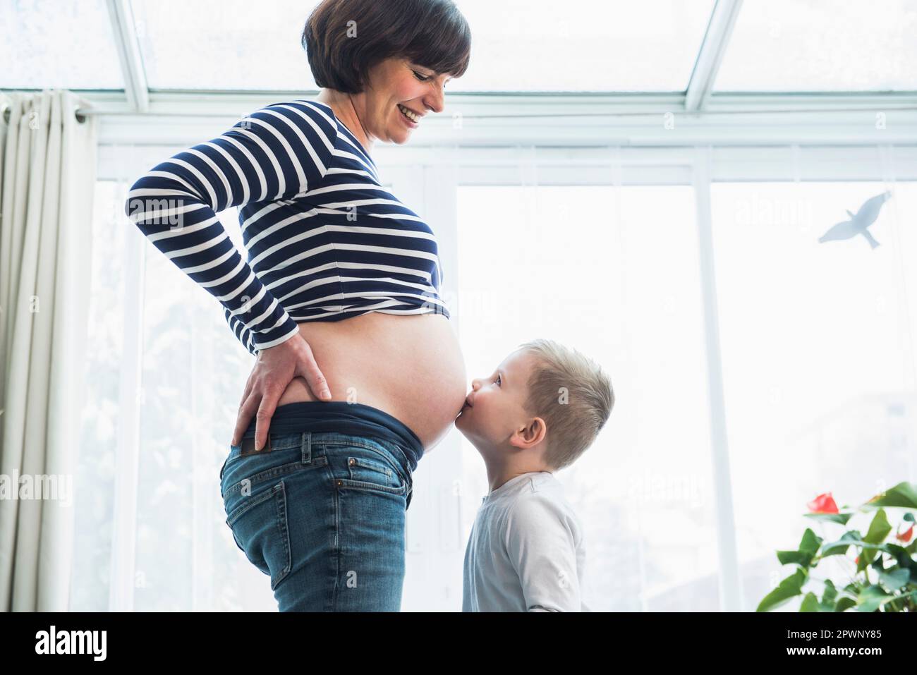 Ein kleiner Junge küsst zu Hause den Magen einer schwangeren Mutter Stockfoto
