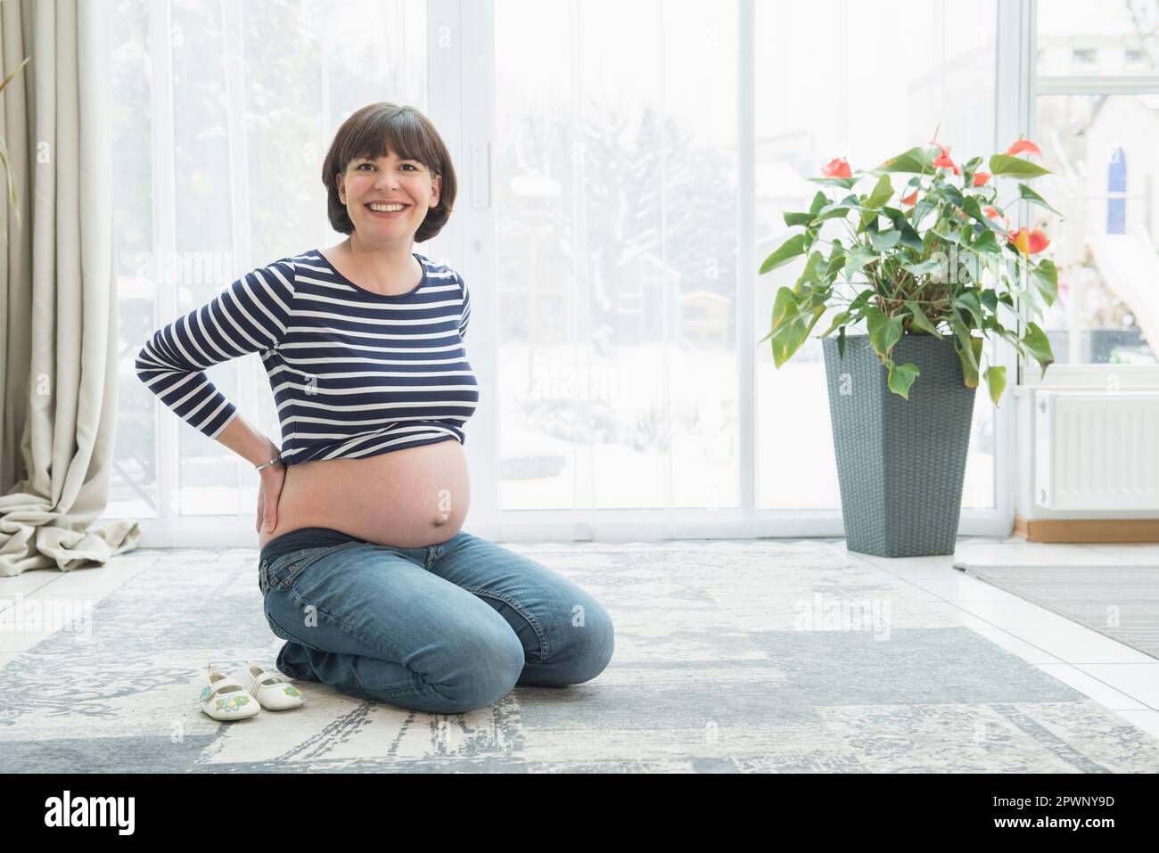 Porträt einer schwangeren Frau, die auf dem Teppich kniet Stockfoto