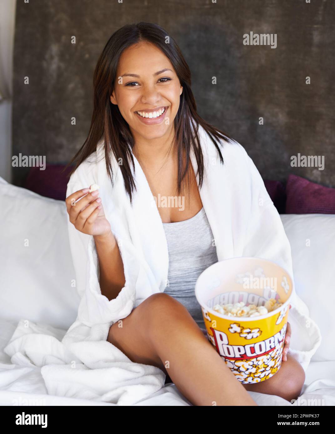 Ihr Heimkino-Snack. Porträt einer jungen Frau, die mit einer Schüssel Popcorn auf ihrem Bett sitzt. Stockfoto