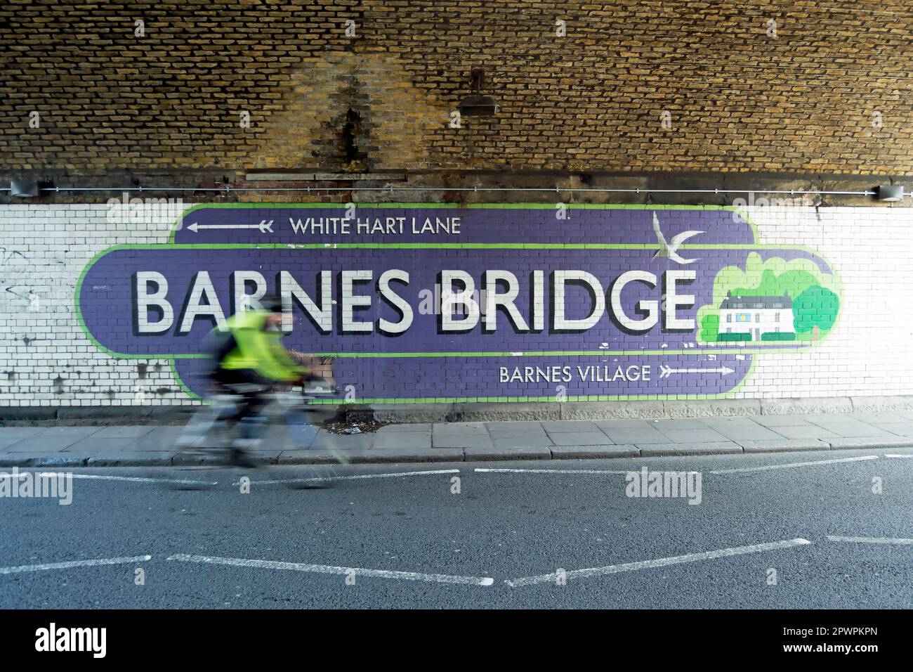 Radfahrer, der in unscharfer Bewegung gesehen wird, passieren ein Wandschild unter der barnes-Eisenbahnbrücke, das Wegbeschreibungen zu lokalen Zielen, barnes, Südwest-london, england, gibt Stockfoto