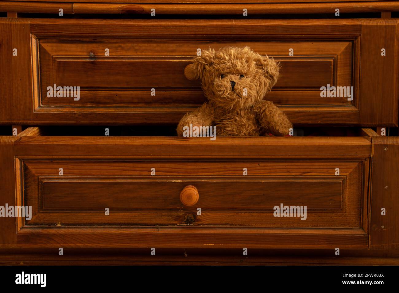 Teddy Braunbär sitzt in einer alten, ausziehbaren Schublade aus Holz im Schlafzimmer als Hintergrund Stockfoto