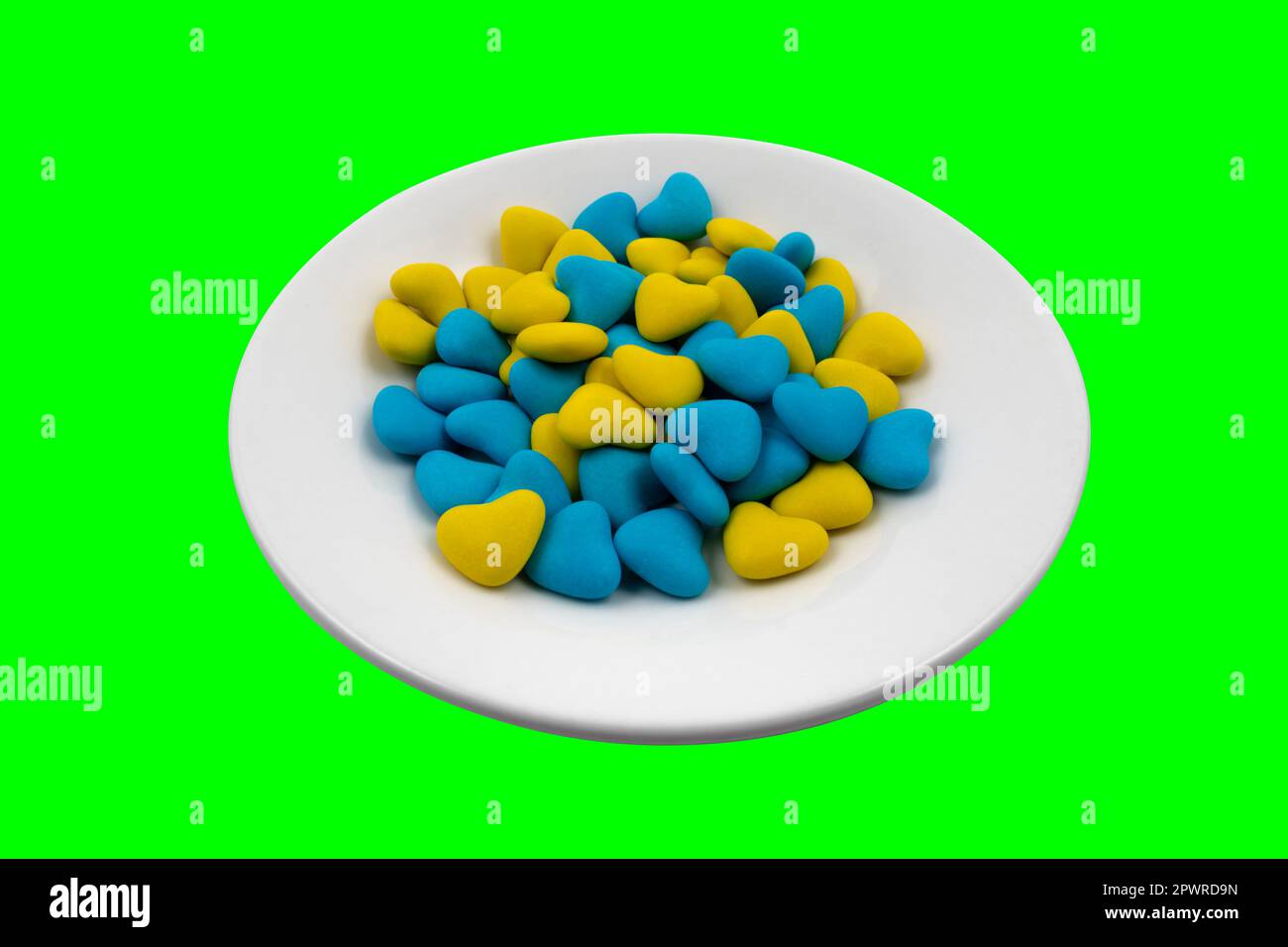 Weiße Platte mit gelben und blauen herzförmigen Süßigkeiten (Nahaufnahme) auf grünem Hintergrund (Chroma-Taste). Staatssymbole der Ukraine. Blick von oben Stockfoto