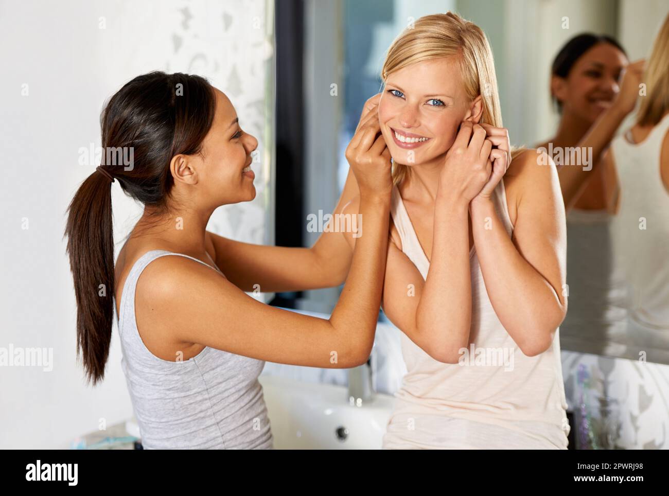 Die sehen toll zu deinem Outfit aus. Eine junge Frau, die ihrem Freund hilft, ihre Ohrringe einzusetzen. Stockfoto
