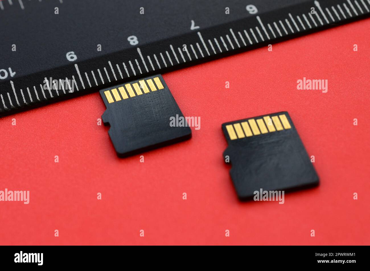 Zwei kleine microSD-Speicherkarten liegen auf rotem Hintergrund neben einem schwarzen Lineal. Ein kleiner und kompakter Daten- und Informationsspeicher Stockfoto