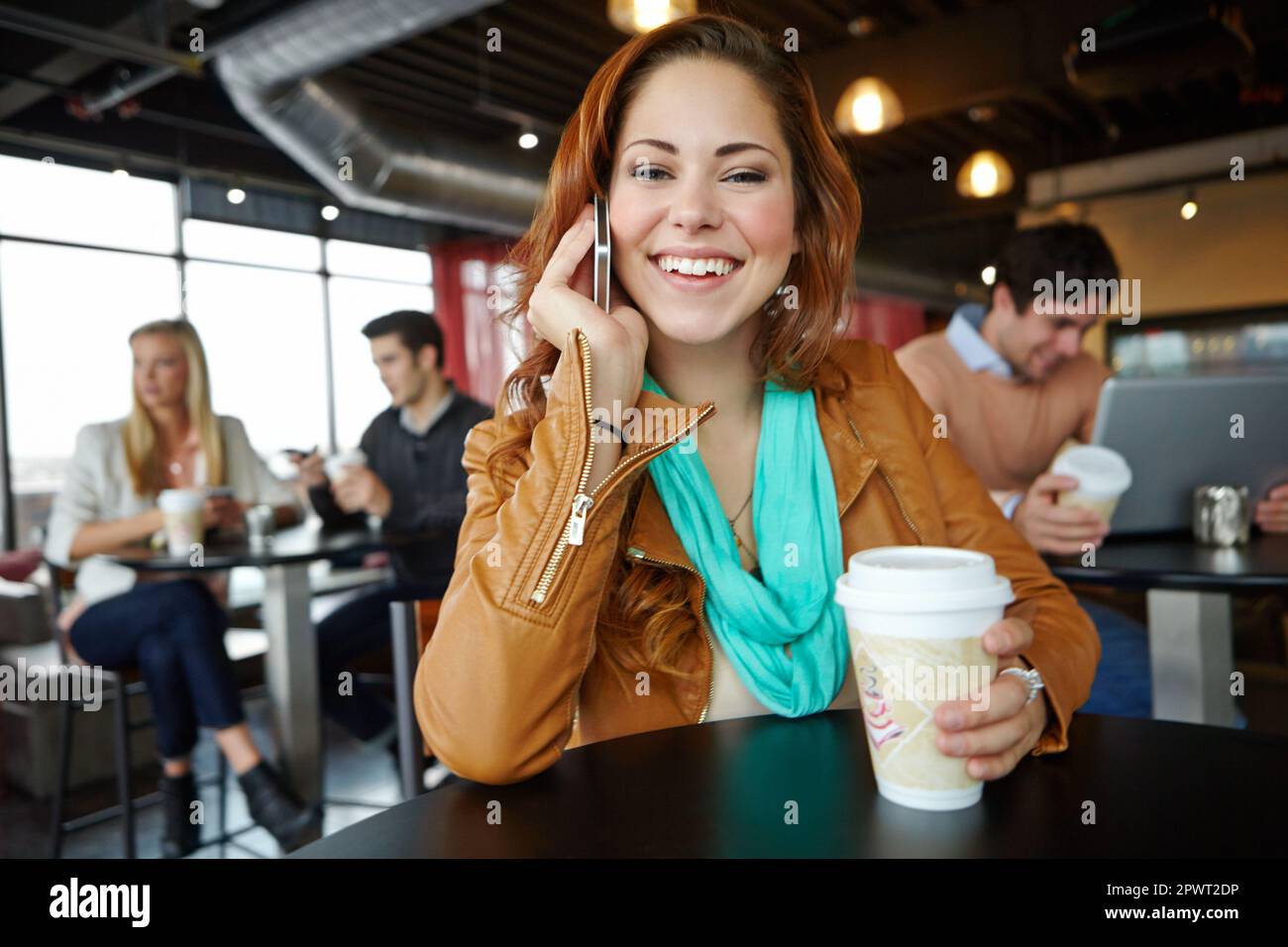Ich trinke schnell einen Kaffee und möchte mitmachen. Eine schöne junge Frau, die ihr Smartphone in einem belebten Café benutzt. Stockfoto