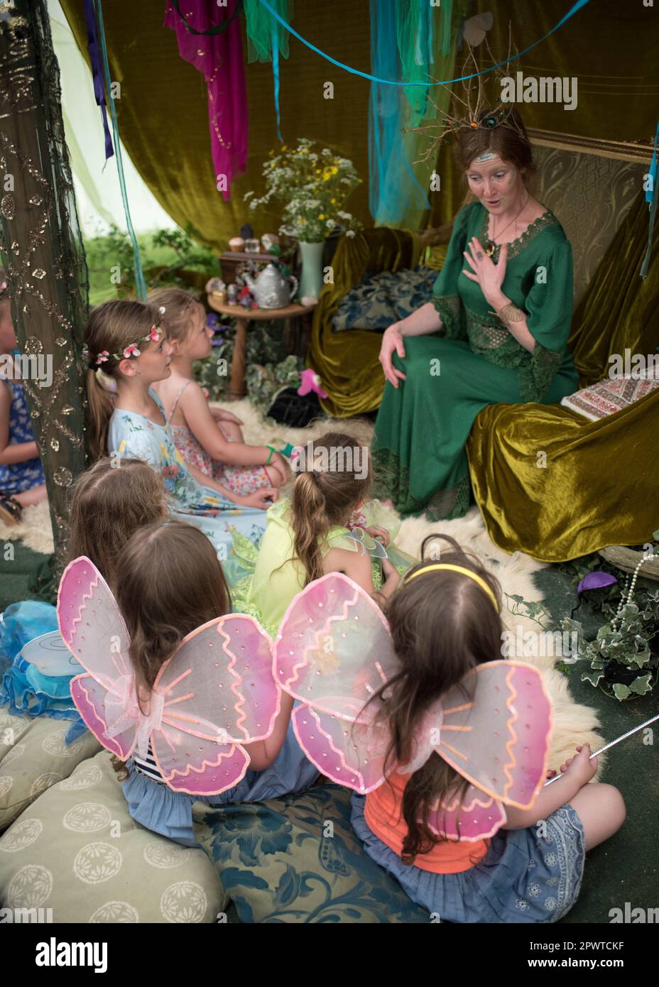 Mädchen mit Feenflügeln, die einem Vortrag einer in Grün gekleideten Dame zuhören, die die Feenkönigin und eine Feenmesse repräsentiert Stockfoto