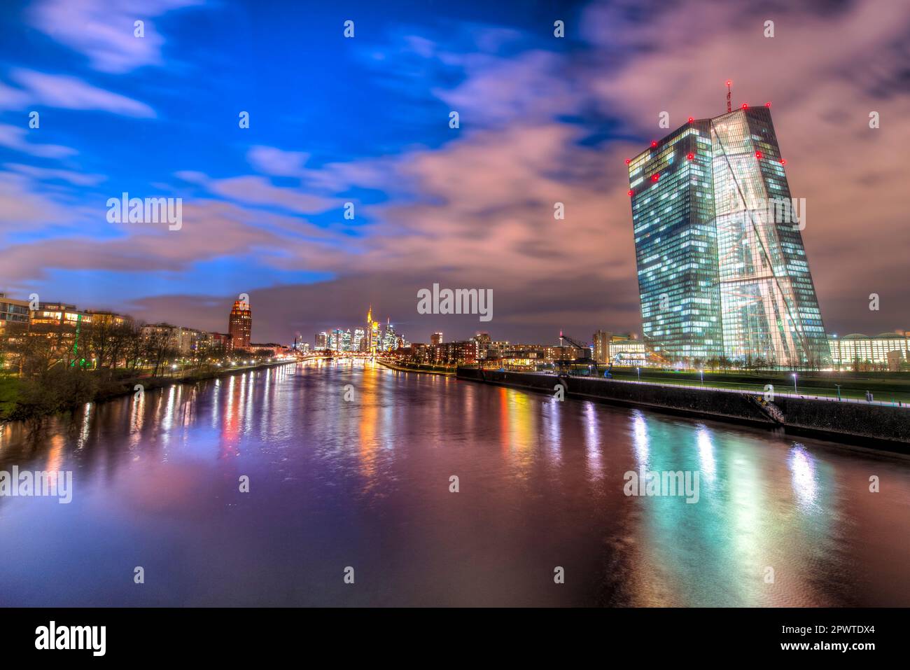 Die EZB (Europäische Zentralbank) in Frankfurt am Main am Abend mit künstlicher Beleuchtung und der Skyline im Hintergrund Stockfoto