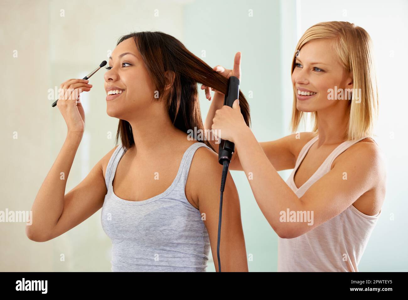 Sie hilft ihr, gut auszusehen. Eine junge Frau, die sich schminkt, während ihr Freund ihr Haar glättet. Stockfoto