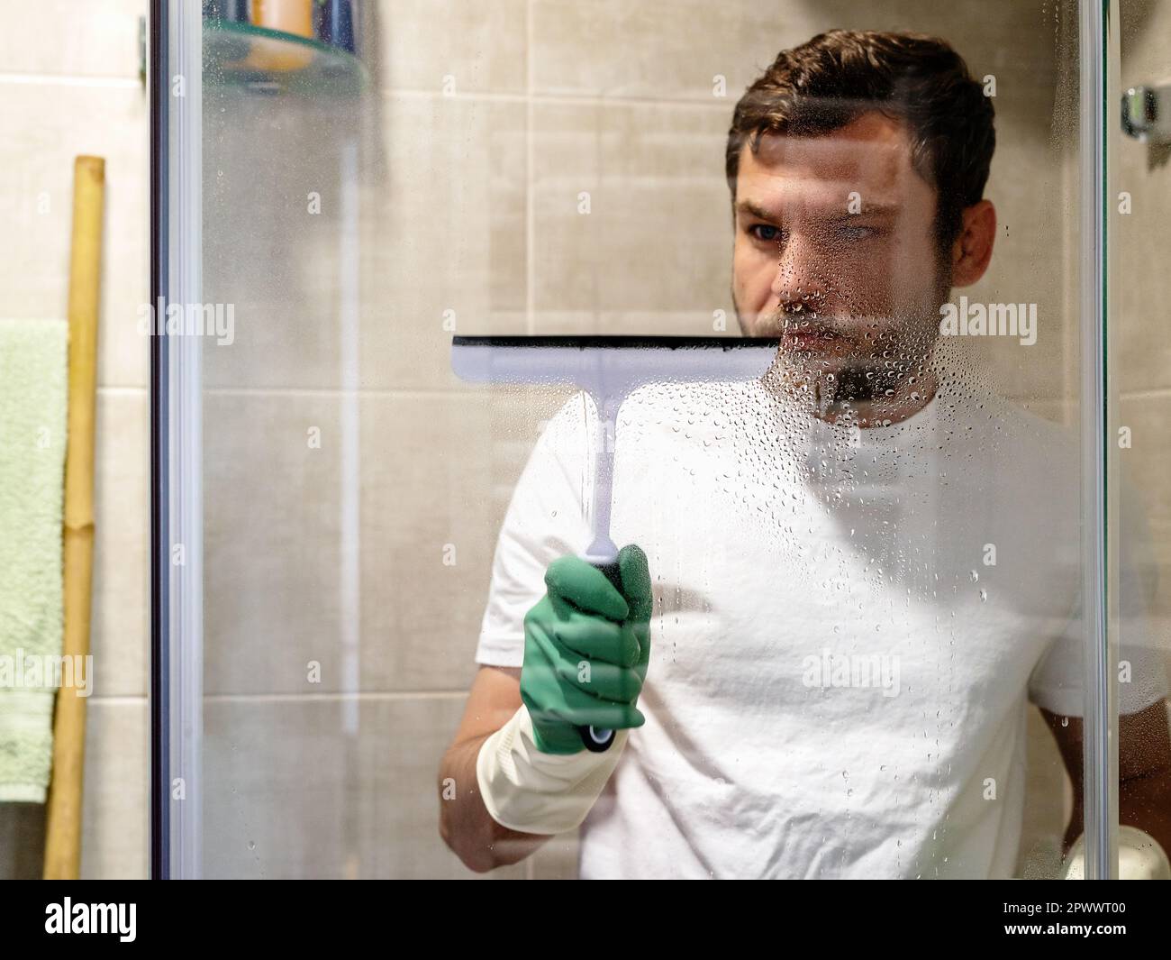 Сleaning Service, man reinigt Glaswände im Badezimmer mit Wischtuch für Glas. Stockfoto