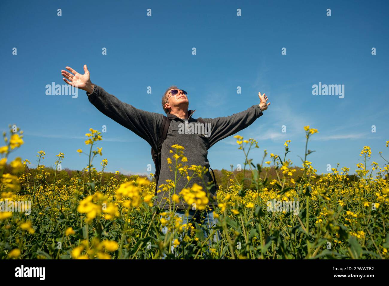 Ein Mann, der mit erhobenen Armen auf einem Feld steht und Freiheit und Landschaft genießt. Geist-Körper-Geist-Konzept. Stockfoto