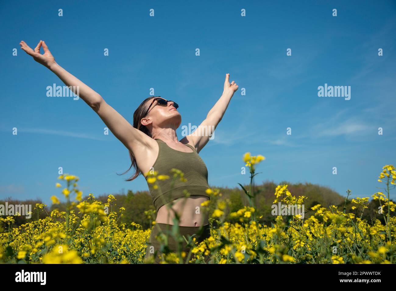 Sportliche Frau mit ausgestreckten Armen auf einem gelben Rapsfeld, Outdoor-Fitness und Yoga-Konzept Stockfoto