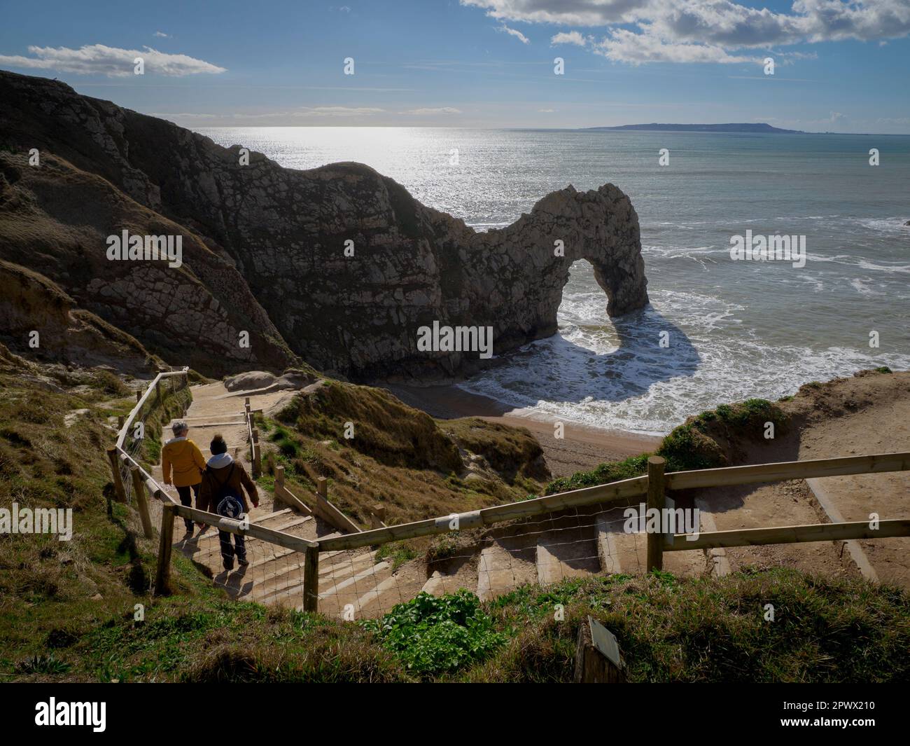 Zwei Personen, die an einem sonnigen Tag im März in Dorset, Großbritannien, die Treppe zum Strand von Durdle Door hinuntergehen Stockfoto
