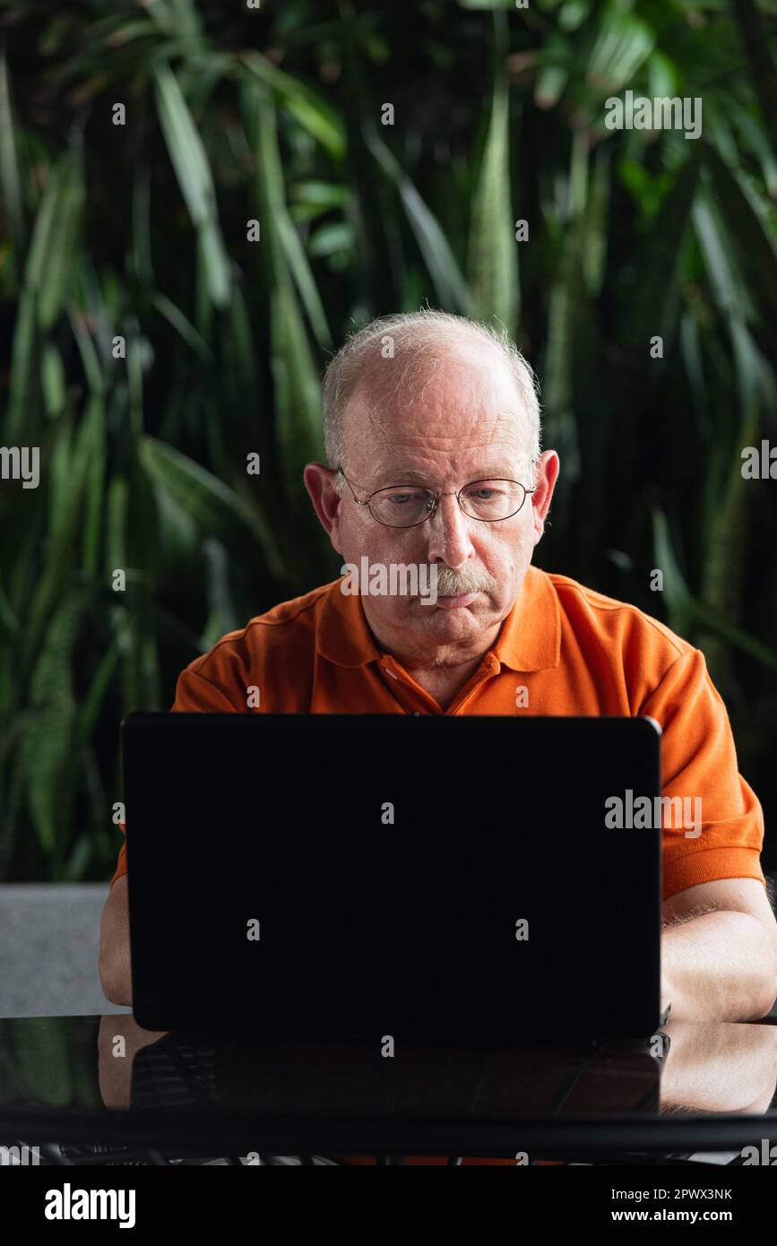 Grauhaariger Senior-Mann mit Schnurrbart, Brille und Laptop-Computer im Freien Stockfoto