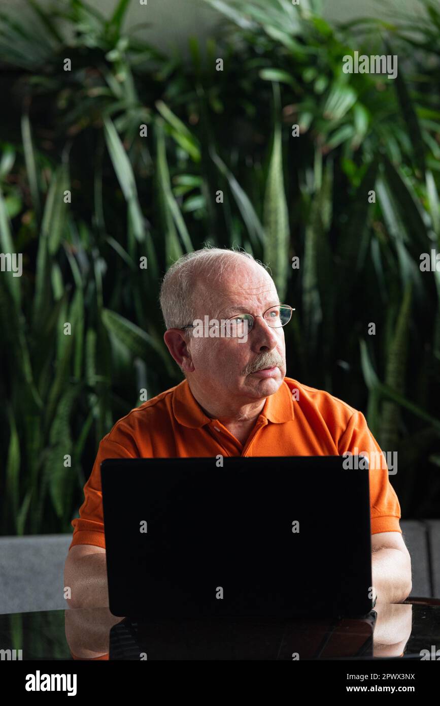 Grauhaariger Senior-Mann mit Schnurrbart, Brille und Laptop-Computer, während er im Freien denkt Stockfoto