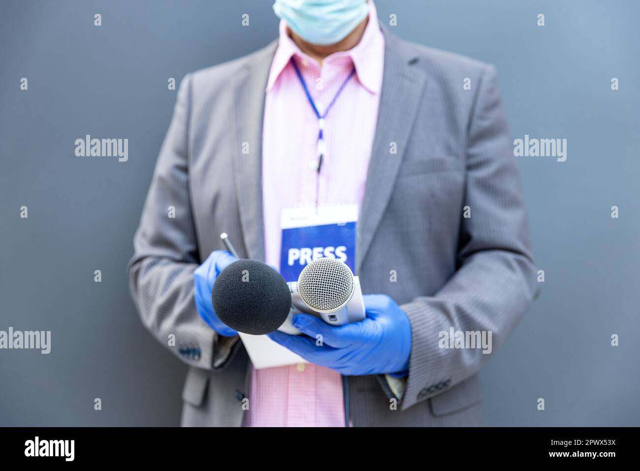 Journalist bei einer Pressekonferenz oder Medienveranstaltung mit Schutzhandschuhen Und Gesichtsmaske gegen Coronavirus COVID-19 Krankheit hält Mikrofon schreiben n Stockfoto