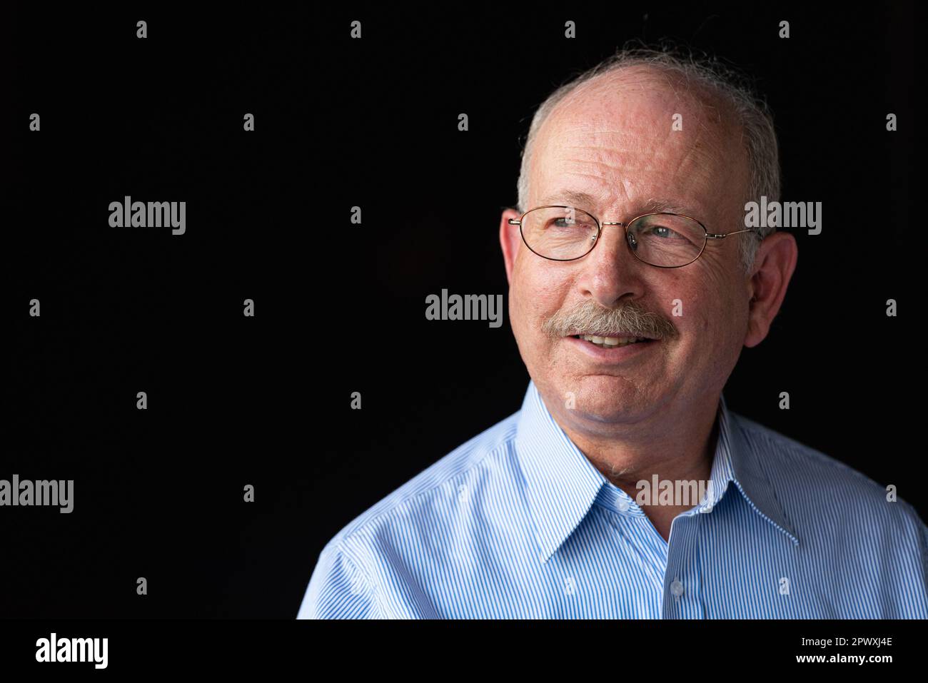Grauhaariger älterer Mann mit lächelndem Schnurrbart und Denken vor schwarzem Hintergrund Stockfoto