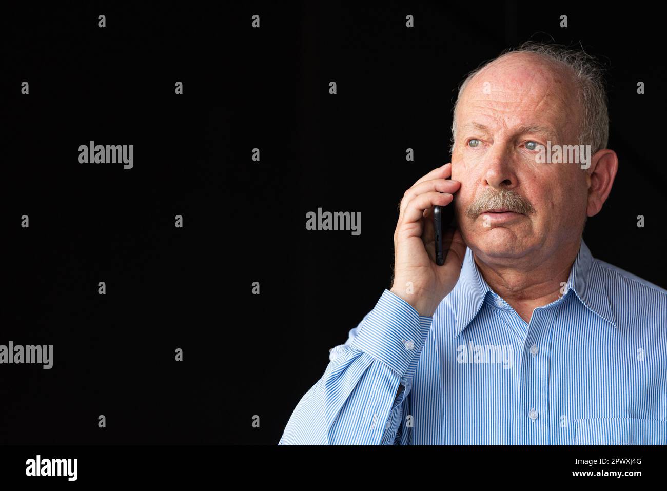 Grauhaariger Senior-Mann mit Schnurrbart, der ein Handy vor schwarzem Hintergrund benutzt Stockfoto