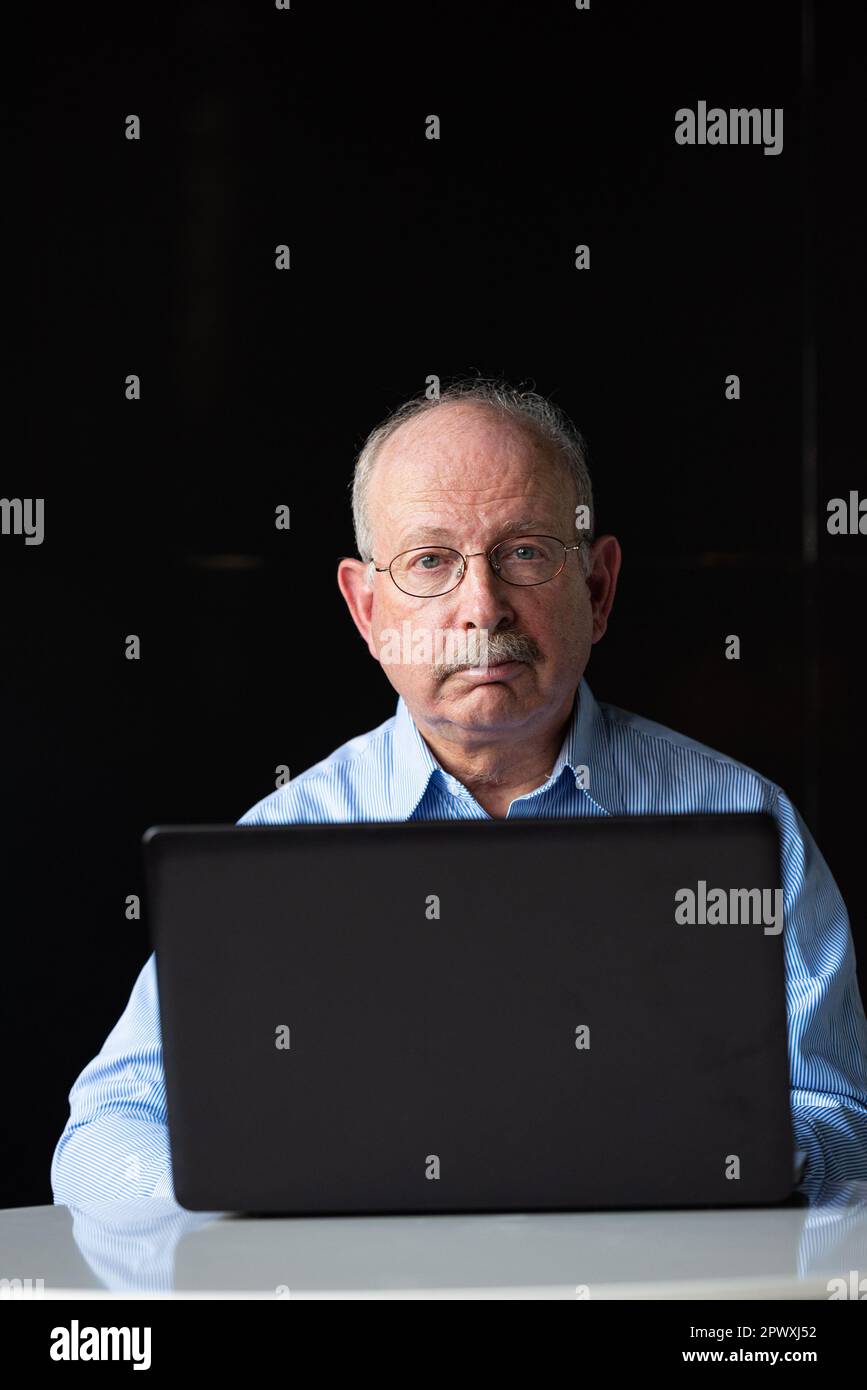 Grauhaariger Senior-Mann mit Schnurrbart, Brille und Laptop-Computer im Sitzen Stockfoto