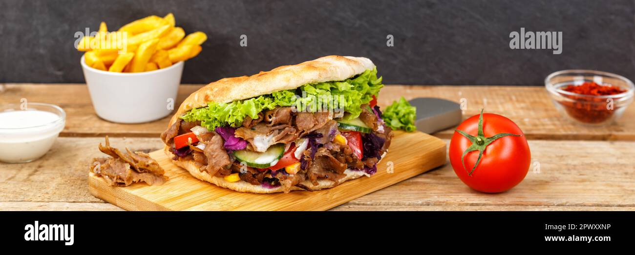 Döner Kebab Döner Kebap Fast-Food-Mahlzeit in Fladenbrot mit Pommes auf einem Holzbrett Panorama-Board Stockfoto