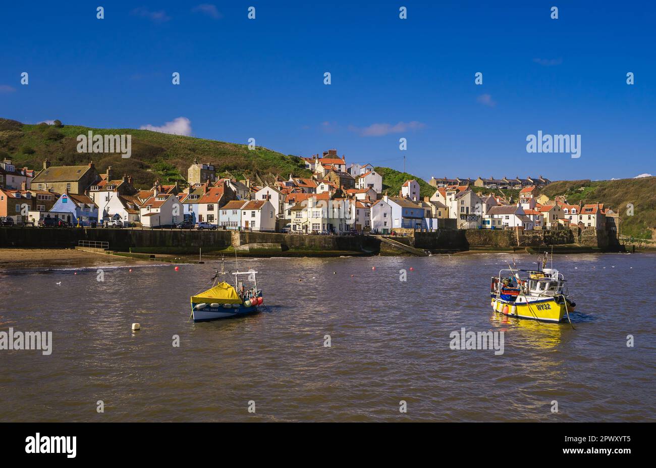 Blick über den Hafen in Staithes bei Flut. Zwei kleine Fischerboote liegen in der Mitte des Hafens vor Anker. Stockfoto