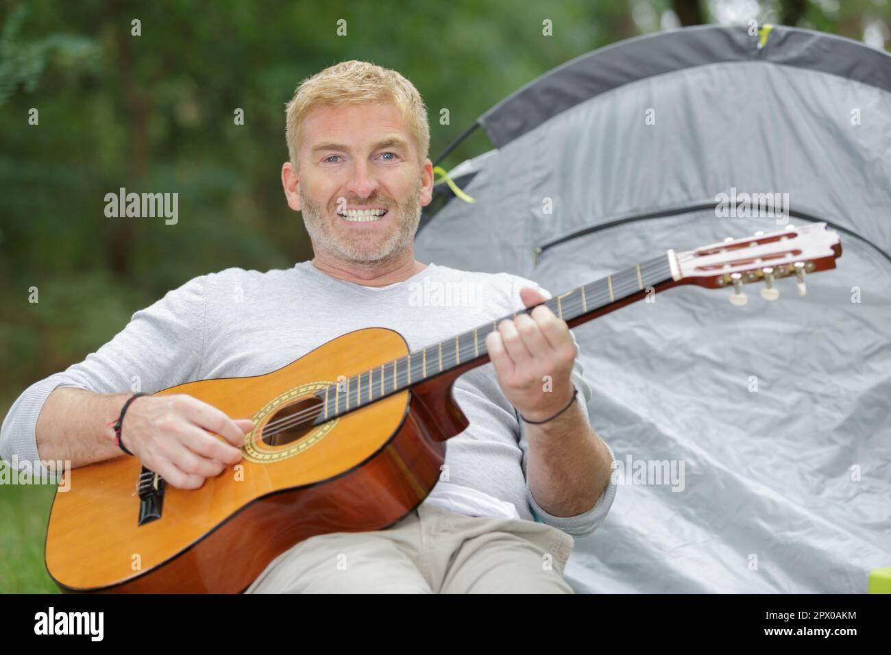 Ein Mann mit Gitarre neben seinem Zelt Stockfoto