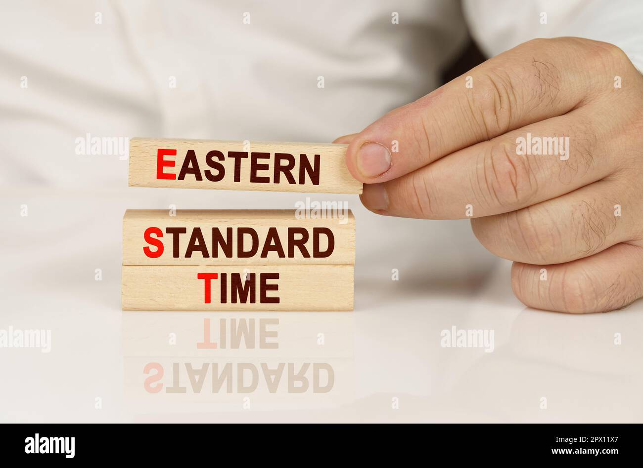 Geschäftskonzept. In den Händen einer Person und auf einer reflektierenden Oberfläche befinden sich Holzblöcke mit der Aufschrift - Eastern Standard Time Stockfoto