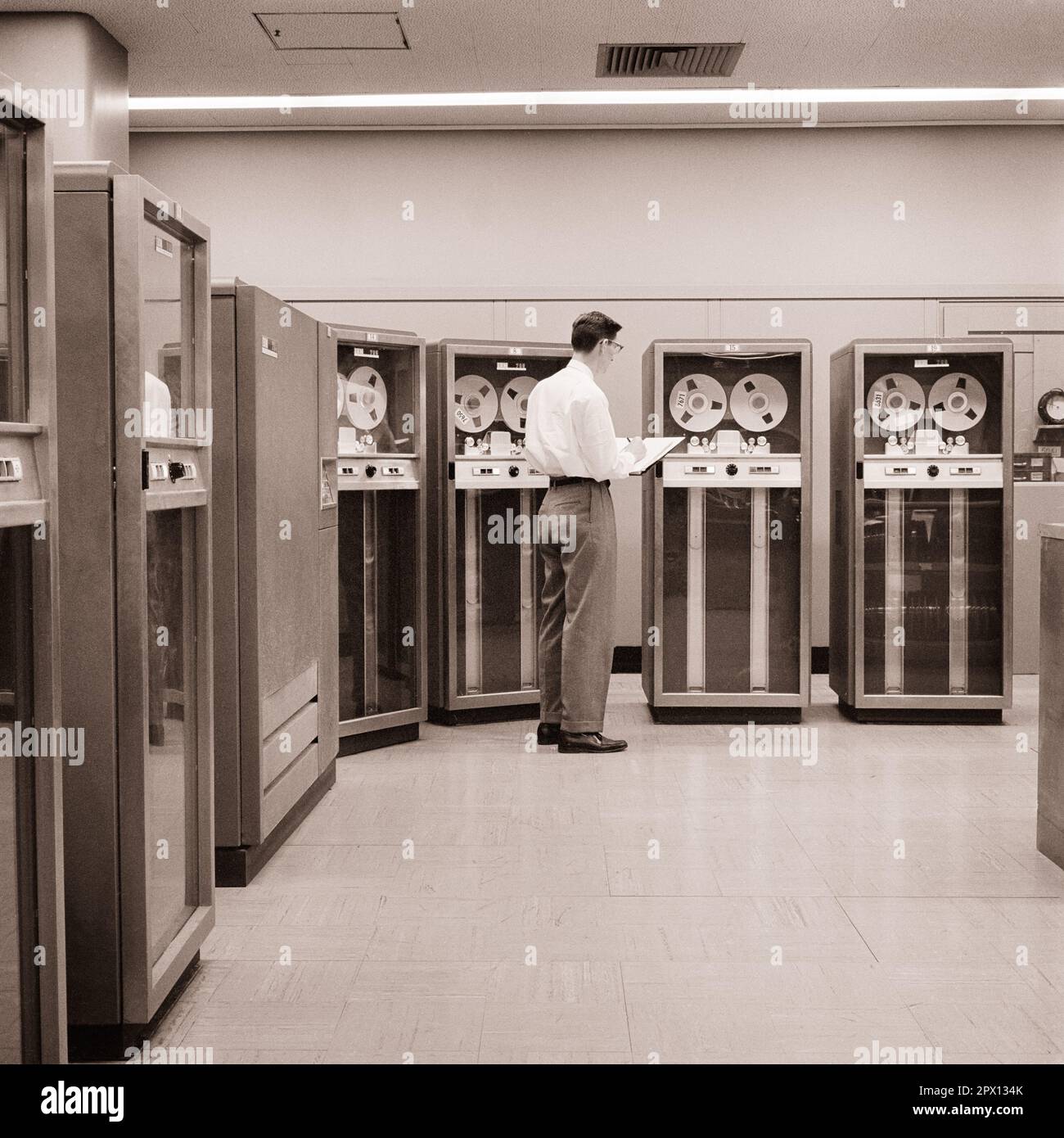 EIN COMPUTERTECHNIKER MIT 1960S MANN STEHT VOR EINEM ARRAY VON IBM-MAGNETBANDLAUFWERKEN DES MODELLS 727 - O2052 HAR001 HARS TECHNIKER MÄNNLICHER BERUF 1953 SCHWARZWEISS-DATEN WEITWINKEL-KOMPETENZ VOR DEM BERUF FERTIGKEITEN FRÜHE VERNETZUNG KARRIERE STARKE FORTSCHRITTE RICHTUNG INNOVATIONSARBEIT UND BESCHÄFTIGUNG BESCHÄFTIGUNG VERBINDUNG KONZEPTIONELLE UNTERSTÜTZUNG FÖRDERT DAS WACHSTUM VON INFRASTRUKTURMITARBEITERN MITTLERE ERWACHSENENEBENE MÄNNER PRECISION SYSTEMS ARRAY SCHWARZ-WEISS WEISSE, KAUKASISCHE ETHNISCHE ÄRA HAR001, DIE MAGNETISCH, ALTMODISCH ARBEITEN Stockfoto