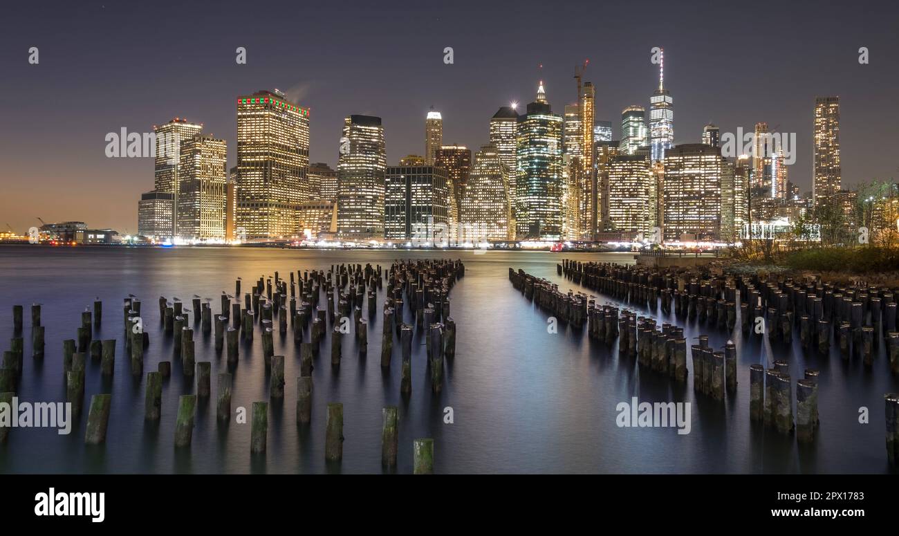 Blick auf Lower Manhattan in der Dämmerung von Brooklyn aus. Der Rest eines alten Piers ist im Vordergrund und die Skyline der Stadt im Hintergrund zu sehen Stockfoto