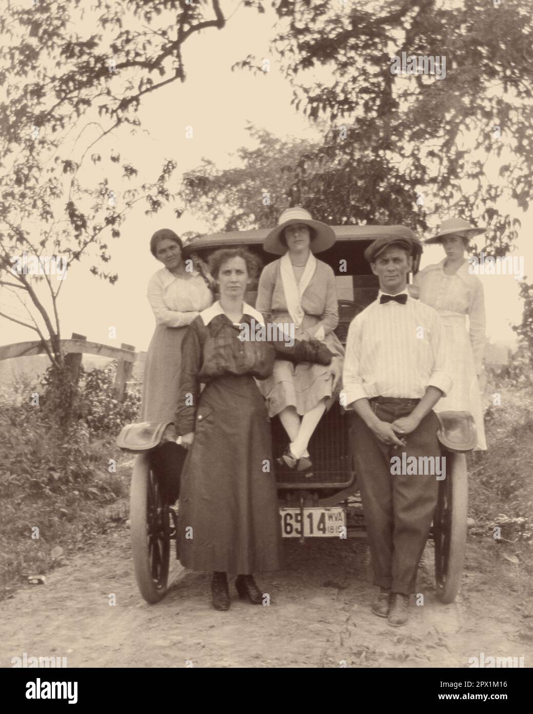 1910S MANN UND FRAU STEHEN VOR DEM AUTO, DREI FRAUEN POSIERTEN UND STANDEN AUF DEM AUTO UND SCHAUTEN ALLE ZU VOR DER KAMERA - O3981 HAR001 HARS-BRÜDER LÄNDLICHER EHEPARTNER ERWEITERTE EHEMÄNNER KOPIEREN WELTRAUMFREUNDSCHAFT VOLLE LÄNGE, HALBE LÄNGE, FRAUEN, AUTO, MÄNNER GESCHWISTER SCHWESTERN TRANSPORT B&W PARTNER BLICKKONTAKT ADVENTURE AUTOS STOLZ GESCHWISTER VERBINDUNG AUTOS STILVOLLE FAHRZEUGE VOR KOOPERATION MITTE ERWACHSENER MITTELERWACHSENER MANN MITTELERWACHSENE FRAU POSIERTE ZUSAMMENSEIN EHEFRAUEN JUNGE ERWACHSENE FRAU SCHWARZ-WEISS WEISSE ETHNISCHE ZUGEHÖRIGKEIT HAR001 HUMORLOS ALTMODISCH Stockfoto