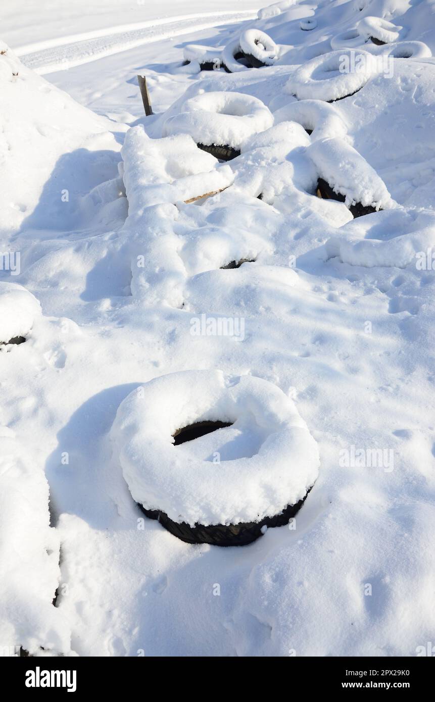 Gebrauchte und entsorgte Autoreifen liegen am Straßenrand und sind mit einer dicken Schneeschicht bedeckt Stockfoto