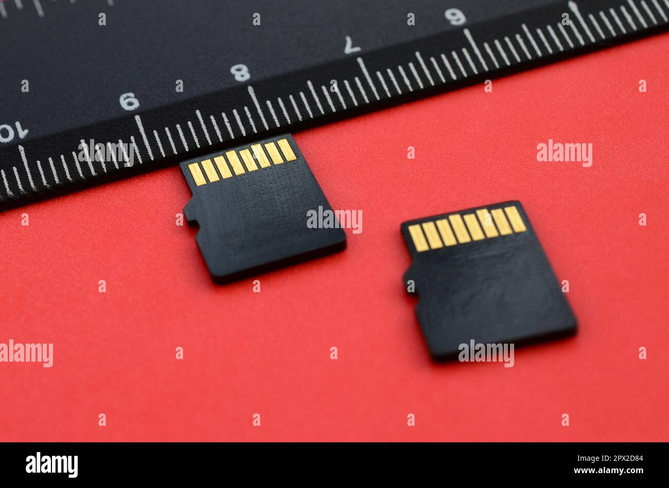 Zwei kleine microSD-Speicherkarten liegen auf rotem Hintergrund neben einem schwarzen Lineal. Ein kleiner und kompakter Daten- und Informationsspeicher Stockfoto