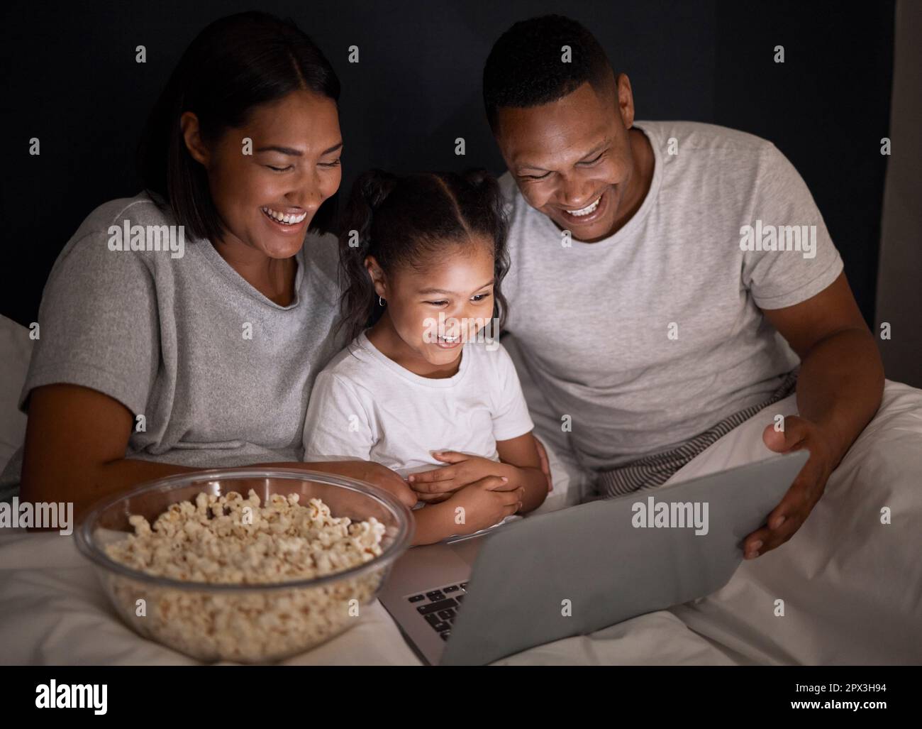 Der Filmabend mit der Familie ist uns wichtig. Ein junges Paar saß mit seiner Tochter im Bett und benutzte nachts einen Laptop Stockfoto