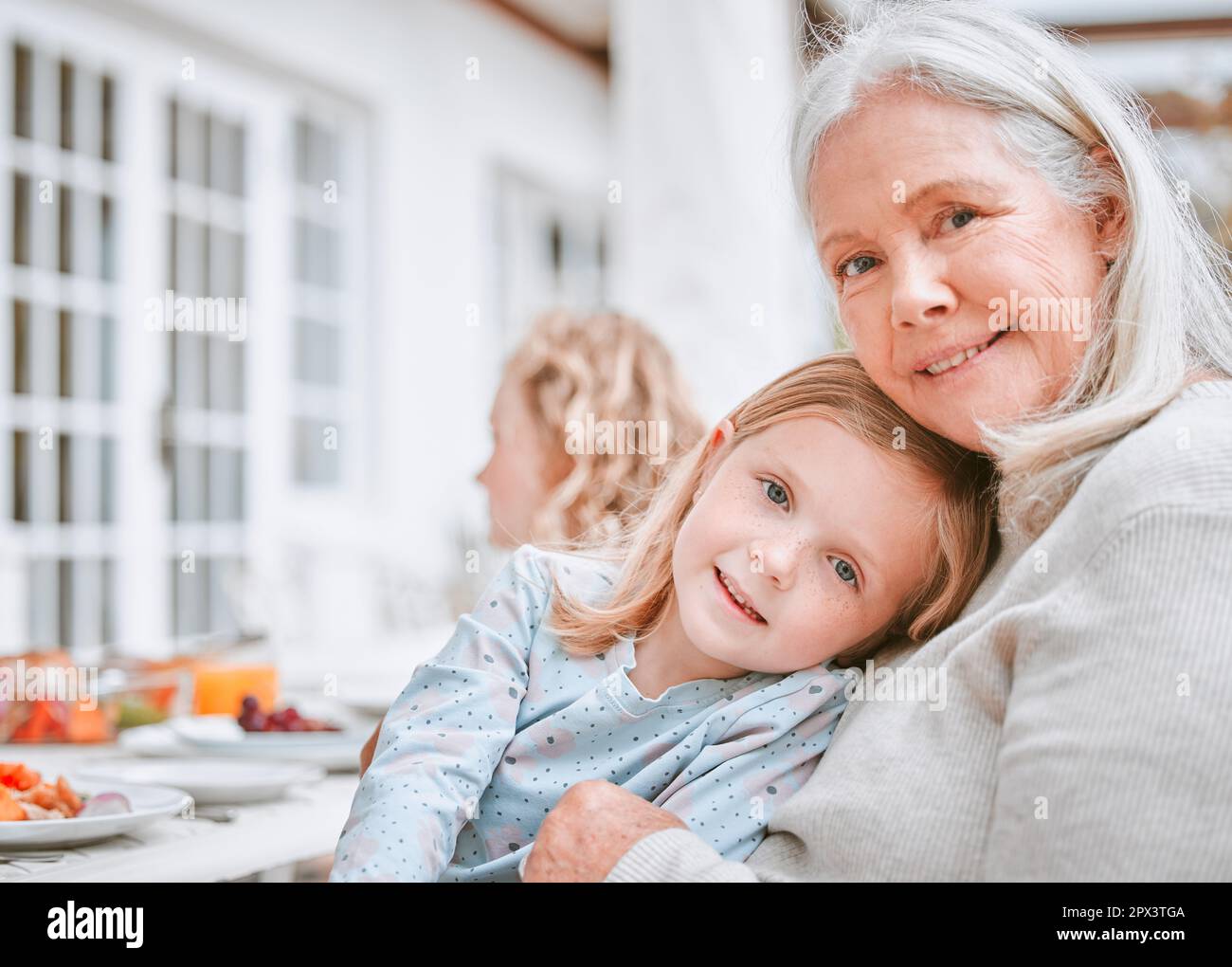 Zuhause ist, wo man geliebt wird. Eine Oma und Enkelin, die draußen an einem Tisch kuscheln Stockfoto