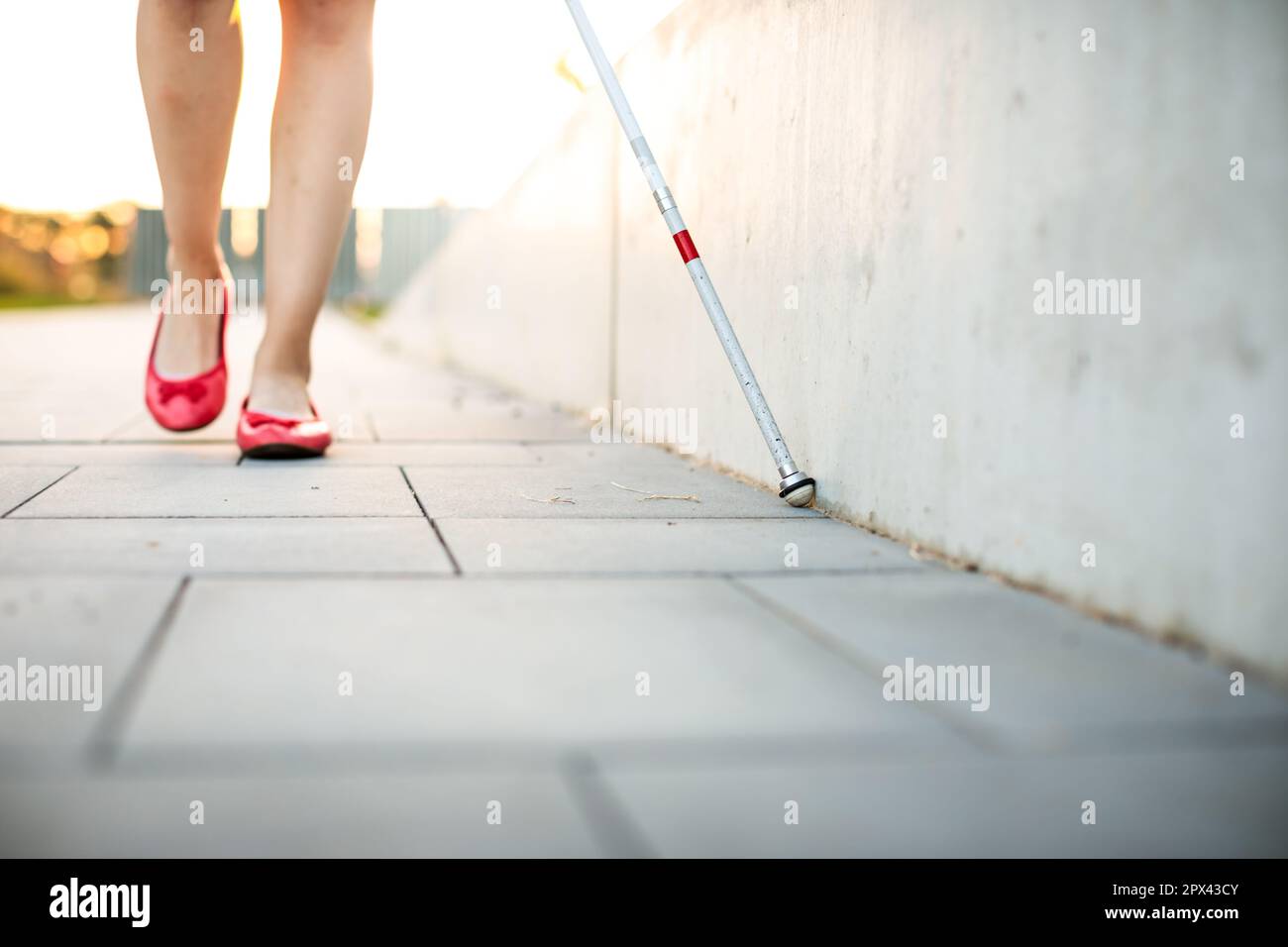 Blinde Frau, die auf den Straßen der Stadt geht, mit ihrem weißen Stock, um den städtischen Raum besser zu navigieren und sicher an ihr Ziel zu gelangen Stockfoto