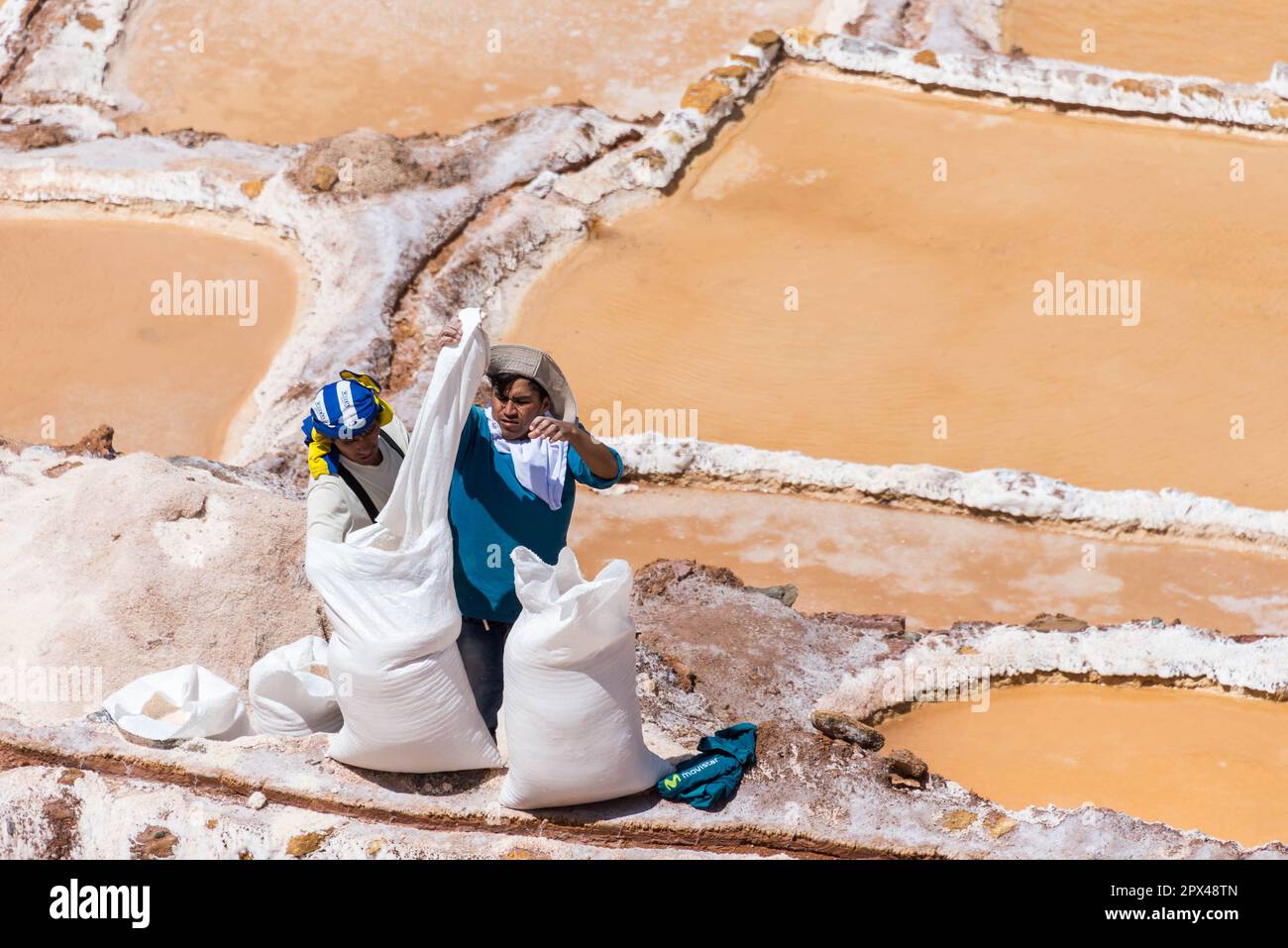Maras, Peru - 19. 2018. Oktober: Zwei Männer sammeln gefiltertes Salz aus der Salinera, um es später zu verkaufen Stockfoto