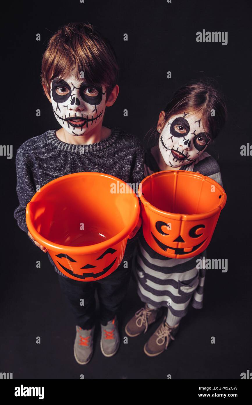 Zwei Kinder mit Totenkopf Make-up halten Kürbis Eimer an Halloween. Stockfoto