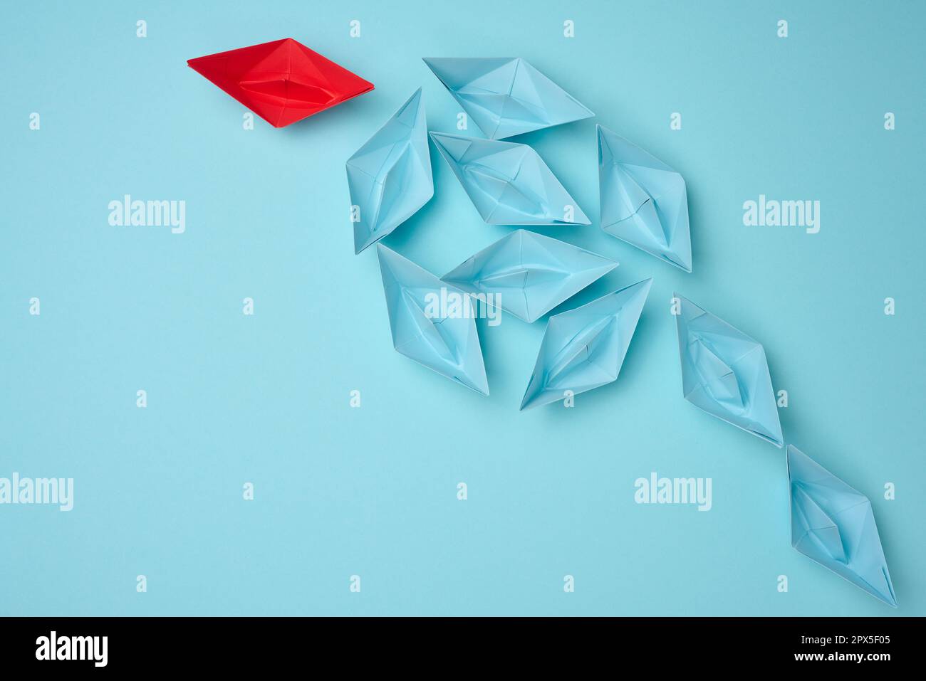 Gruppe blauer Papierboote, die in eine Richtung fahren, und ein roter, einer in die entgegengesetzte Richtung. Der Begriff Individualität, Einzigartigkeit und Tal Stockfoto