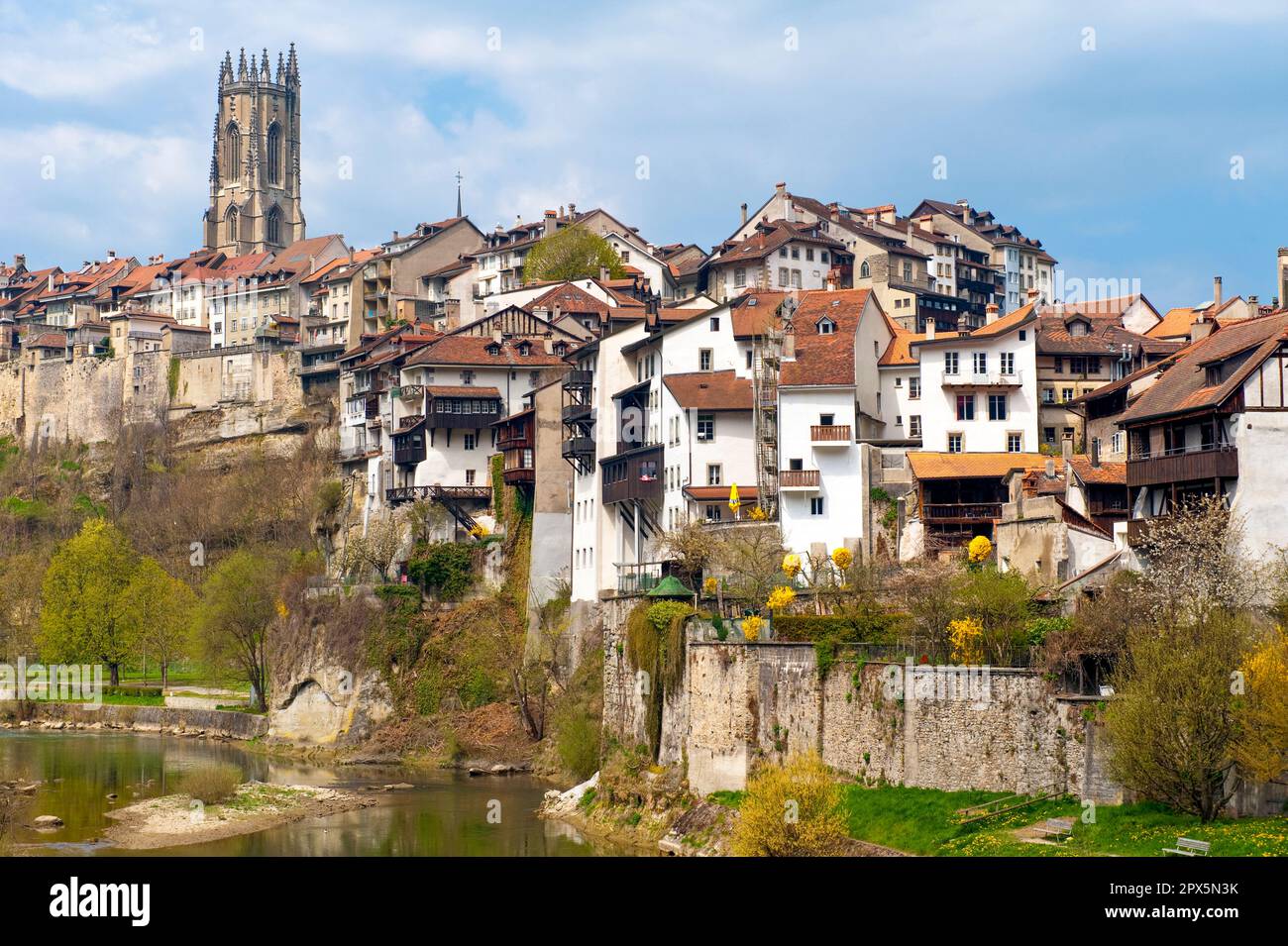 Eine Reihe von Häusern mit dem Turm der Nikolaikirche auf einem Felsen am Ufer der Saane in der Altstadt von Freiburg, Schweiz Stockfoto