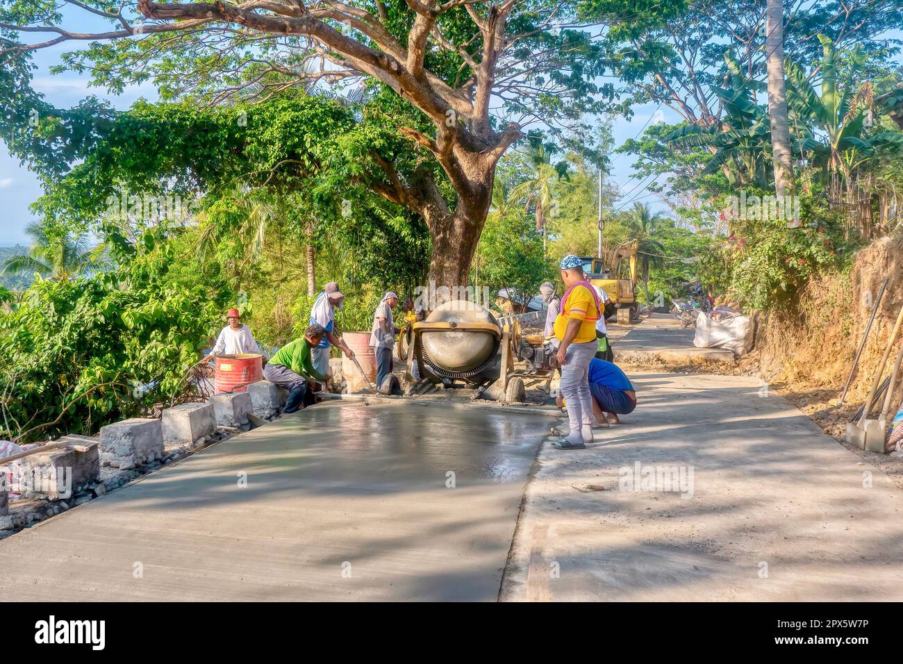 Puerto Galera, Philippinen - 22. April 2023. Philippinische Arbeiter mischen und gießen eine Betonplatte auf einem Straßenbauprojekt in der Nähe des Dorfes Baclayan. Stockfoto