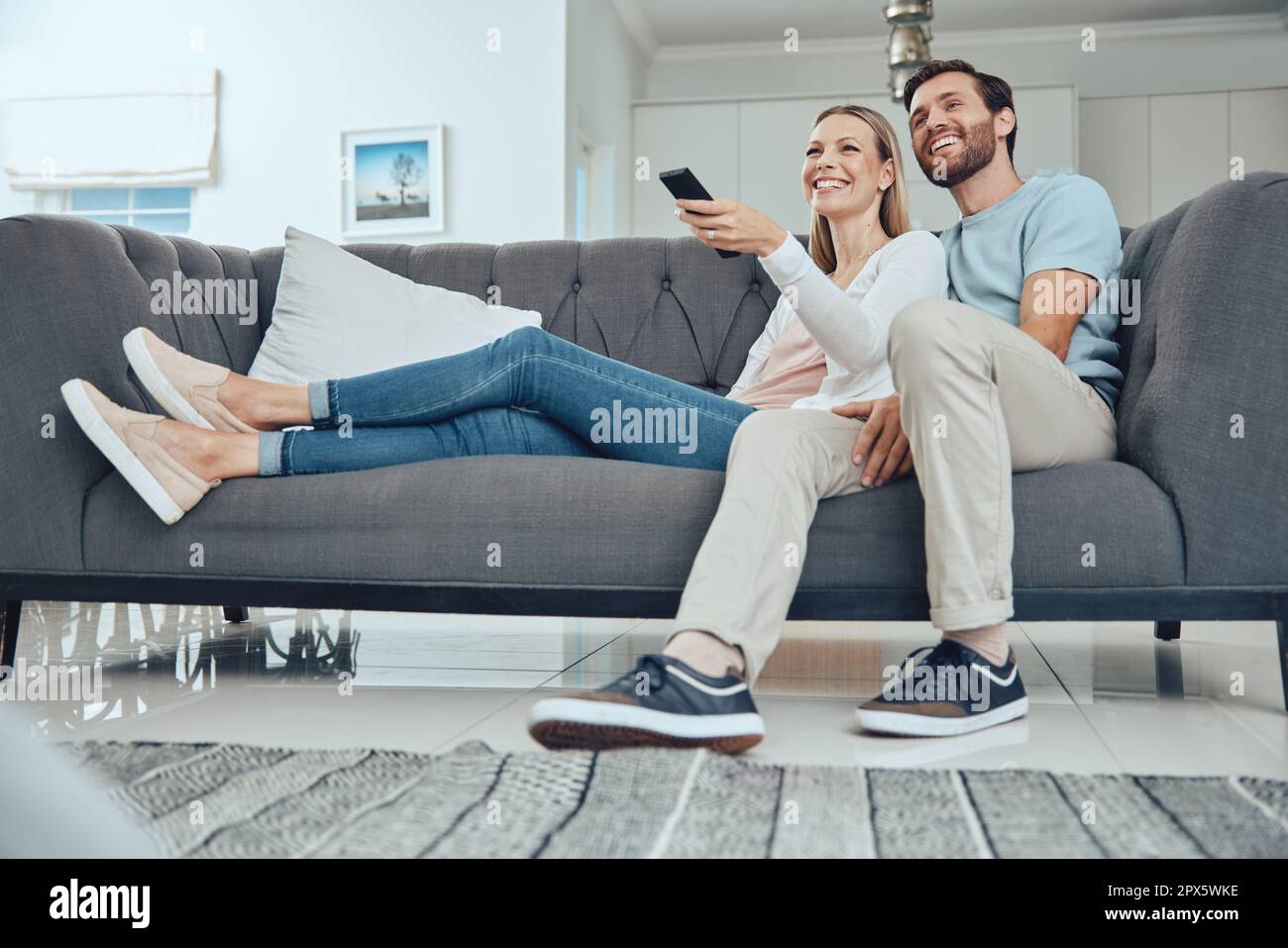 Paare, Sofa und entspannen Sie sich mit tv-Fernbedienung, Lächeln und Glück im Wohnzimmer, um sich mit Liebe zu verbinden. Glückliches Paar, Couch und Comedy im Fernsehen, St. Stockfoto