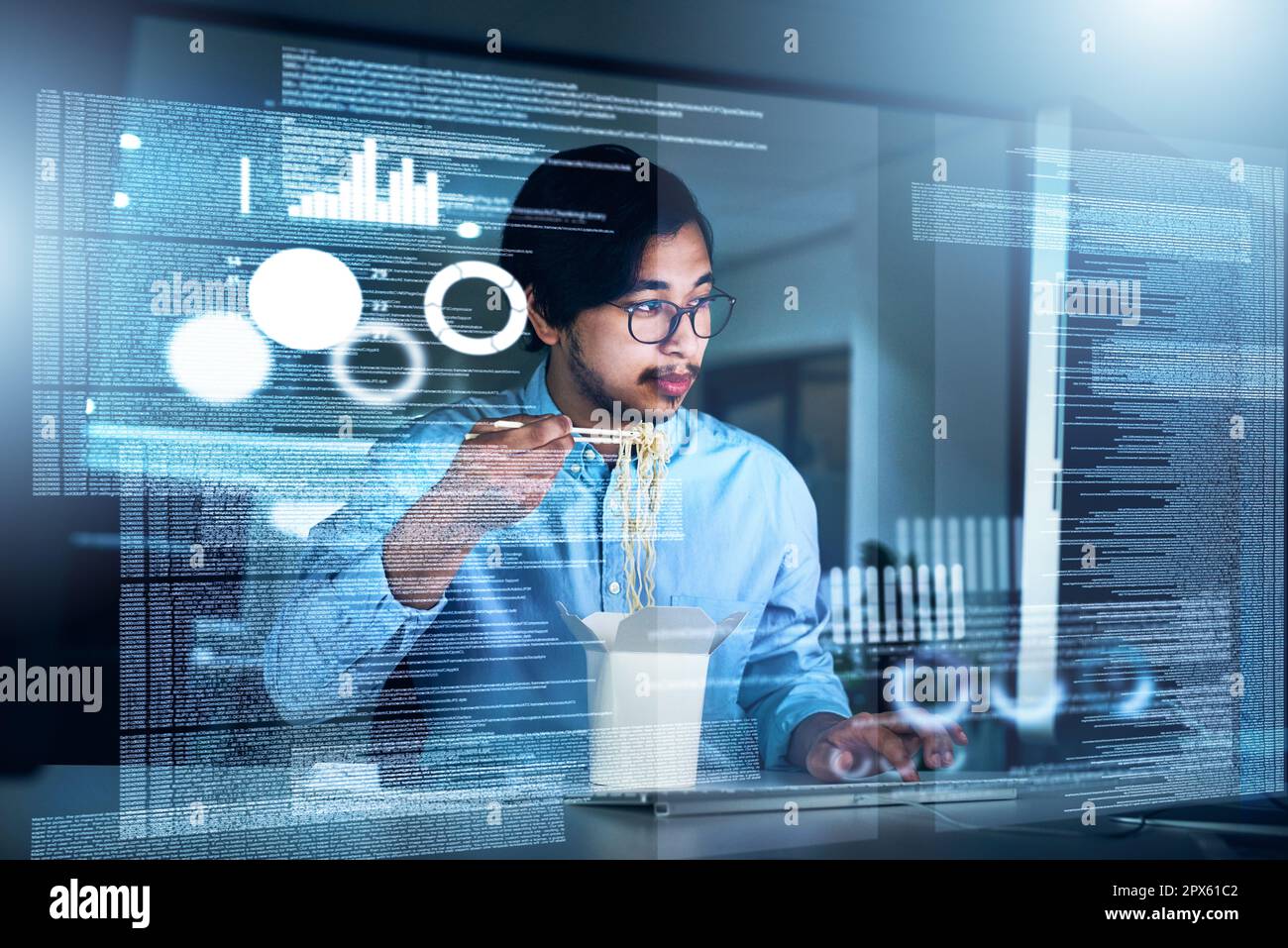 Auftanken während der Arbeit. Ein fokussierter junger Programmierer, der an einem Computer arbeitet, während er abends im Büro Nudeln isst Stockfoto