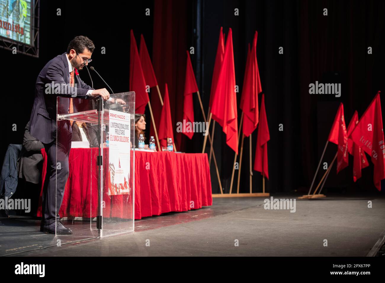 Ein Aktivist von Lotta Comunista auf der Bühne während seiner Rede mit den roten Fahnen im Hintergrund. Wanderarbeiter aus den römischen Vororten waren Ehrengäste bei der traditionellen Feier zum Mai, die Lotta Comunista, die exparlamentarische, internationalistische Bewegung, jedes Jahr im Teatro Brancaccio in Rom organisiert. Die wichtigsten Leitmotive der diesjährigen Konferenz waren ein entschiedenes Nein zum Frieden mit Waffen, die entschiedene Ablehnung jeglicher Form von Fremdenfeindlichkeit und die Notwendigkeit, die Proletarier der ganzen Welt zu vereinen. Stockfoto