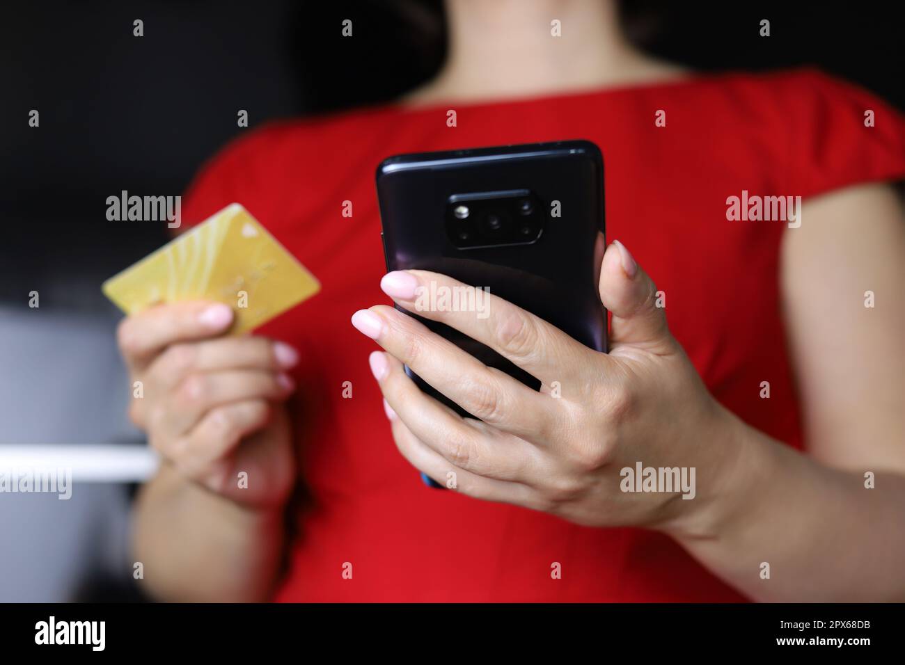 Eine Frau in rotem Kleid, die ein Smartphone und eine Kreditkarte in den Händen hält. Konzept von Online-Zahlungen, -Einkäufen und -Transaktionen Stockfoto