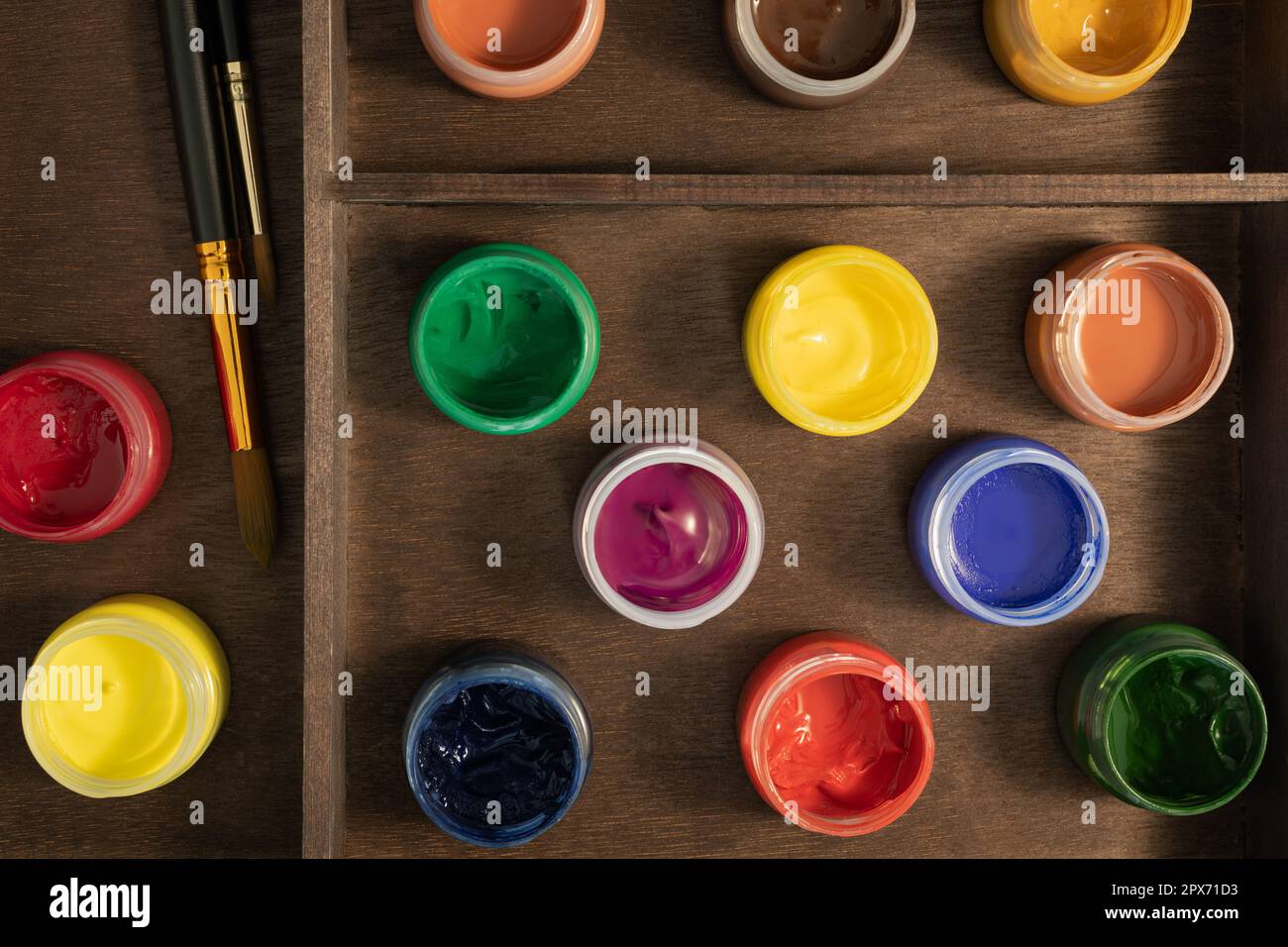 Gouache-Farben und -Pinsel auf Holzständer, flach liegend. 13 offene Flaschen künstlerischer Gouache-Farbe und zwei synthetische Pinsel in Staffelei-Box Stockfoto